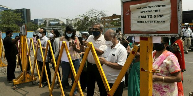 Menschen warten vor einer gelben Absperrung vor einem geschlossenen Impfzentrum in Mumbai