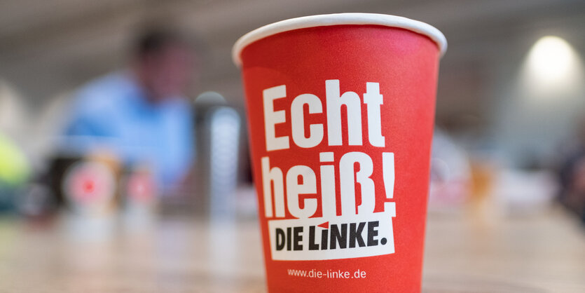 Ein roter Pappbecher steht auf einem Tisch, darauf steht: Echt heiß, die Linke