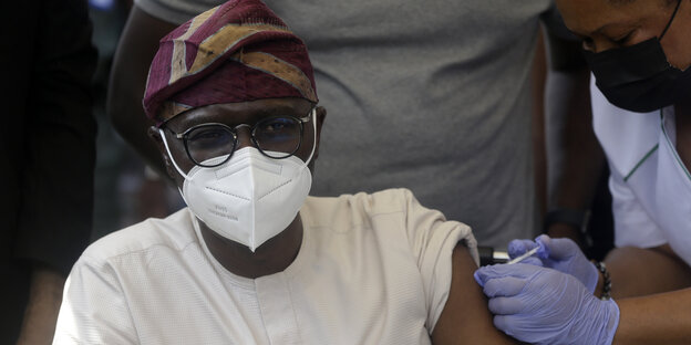 Mann mit Maske bekommt Impfspritze mit Astrazeneca