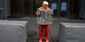 Als Trump verkleideter Demonstrant mit Zeitung in Gefängniskleidung.