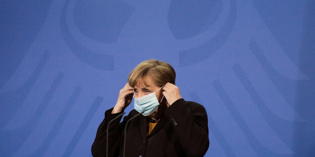 Merkel setzt sich eine Maske auf