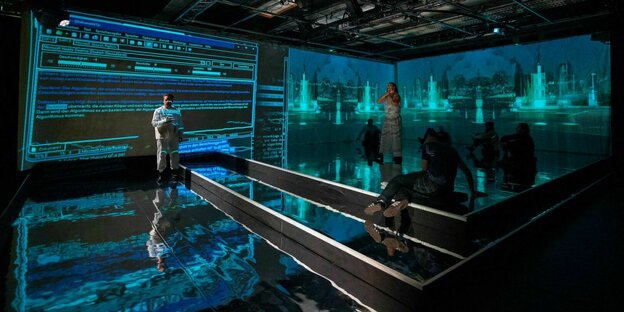 Szene aus dem Stück "Prometheus Unbound" von CyberRäuber: Schauspieler auf einer in blaues Licht getauchten Bühne, das von Videoprojektionen an den Wänden stammt