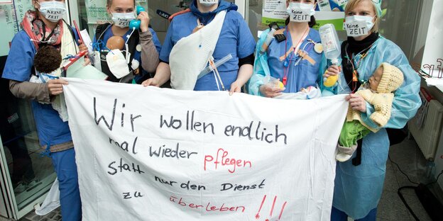 PflegerInnen an der Charité streiken und halten ein Plakat hoch, auf dem steht: "Wir wollen endlich wieder mal pflegen, statt nur den Dienst zu überleben!"