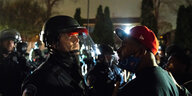 Ein Demonstrant mit roter Käppi spricht mit einem Polizisten in Schutzkleidung und -helm