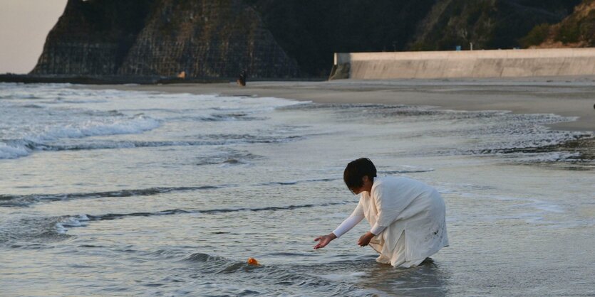 Eine Frau legt Blumen an einem Strand ab.