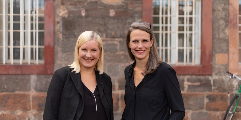 Eine blonde junge Frau und eine dunkelhaarige junge Frau stehen vor dem Hessischen Landestheater Marburg, das sie als Intendantinnen leiten