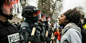 Eine junge Frau brüllt bewaffnete Polizisten an, die sich vor ihr aufgebaut haben