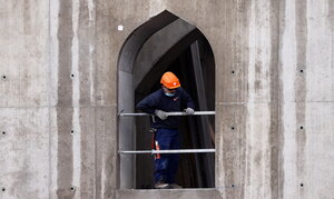 Ein Bauarbeiter mit orangem Schutzhelm schaut aus einem Rohbau für eine Moschee hinaus