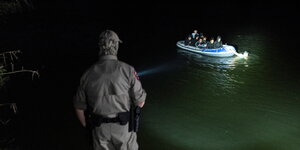 Ein Uniformierter leuchtet mit einer Taschenlampe auf ein Schlauchboot mit Menschen.