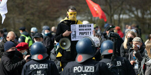 Ein Mann mit gelber Maske steht vor Polizisten in Schutzausrüstung