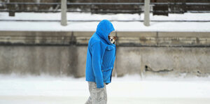 Ein Mann mit blauer Jacke und Hund spaziert durch den Schnee.
