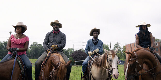 Vier Schwarze Reiter in Westernkleidung, zwei Männer und eine Frau, aufgereiht nebeneinander schauen sie dem Betrachter frontal entgegen