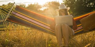 Frau mit Notebook in einer Hängematte im Garten.