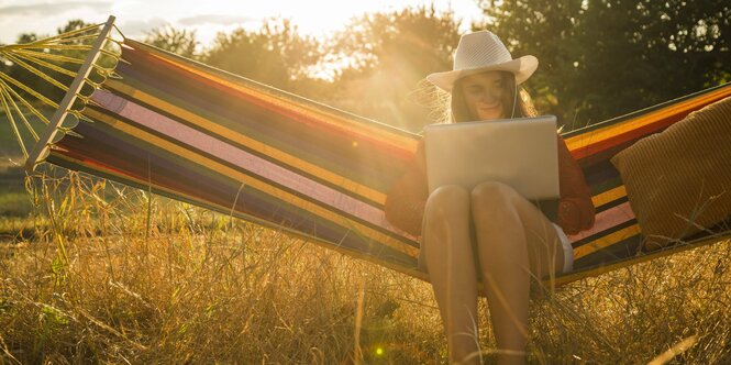 Frau mit Notebook in einer Hängematte im Garten.