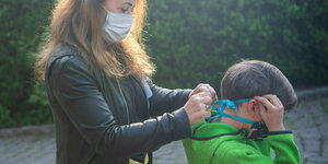 Eine Frau hilft einem Kind eine Maske aufzusetzen.