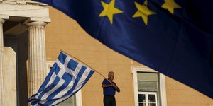 Ein Mann schwenkt eine griechische Flagge, im Vordergrund weht eine europäische Flagge.