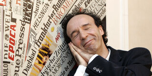 Roberto Benigni, den Kopf lächelnd auf die gefalteten Hände gelegt