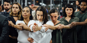 Eine Gruppe Menschen fasst sich an den Armen und bildet ein Dreieck (Performance "Beyond Control" von Carolina Caycedo)