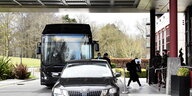 Ein Bus und ein PKW vor einem Luxushotel - eine Passagierin geht Richtung Hotel und hält Unterlagen vor's Gesicht