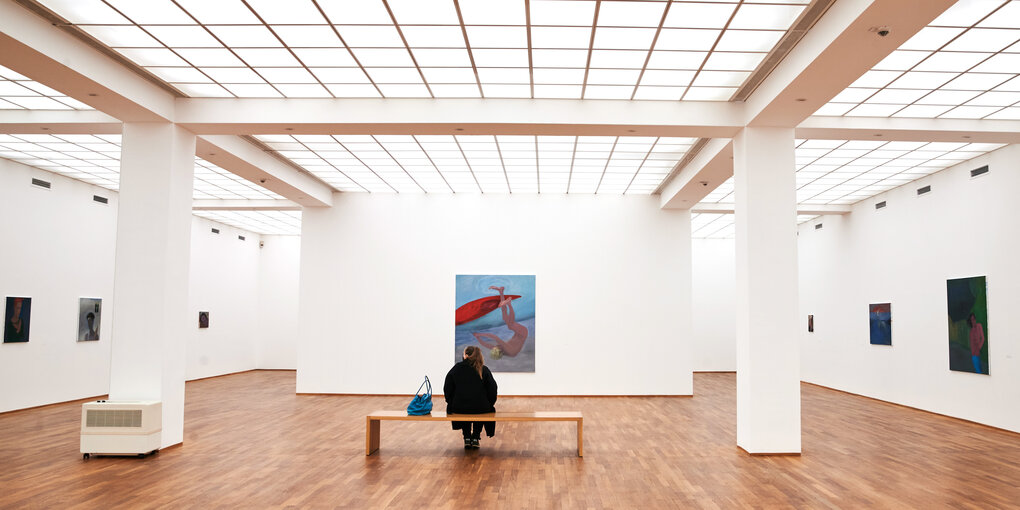 Das Bild zeigt eine Frau auf einer Bank im ansonsten leeren Kunstmuseum Hamburger Bahnhof in Berlin.