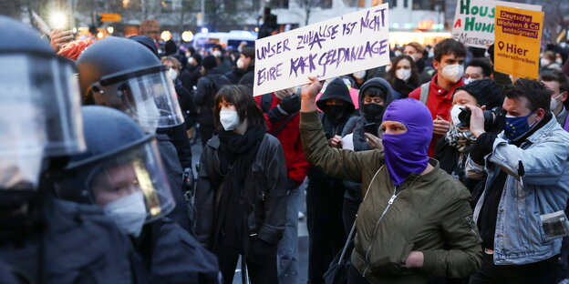 Demosituation: links Polizei mit Helmen auf den Köpfen, rechts eine Demonstrierende mit Schild gegen Mietenwahnsinn