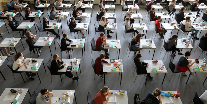 Abiturenten sitzen an Einzeltischen in einem Saal.