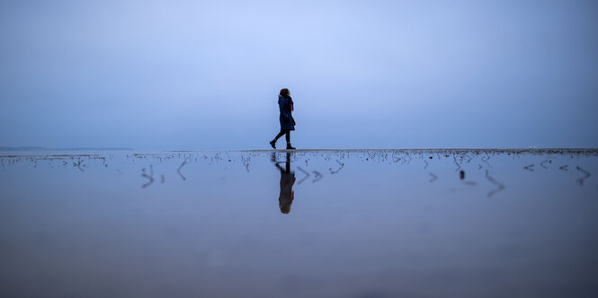 Eine Frau läuft alleine über eine Sandbank am Wohlenberger Wieck an der Ostseeküste.