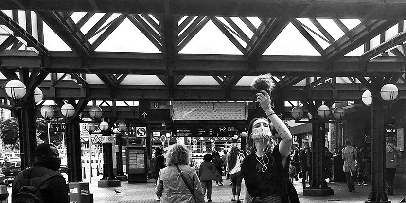 Eine Frau steht am Hamburger Hauptbahnhof und hält ein Mikrofon in die Luft.