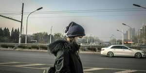 Eine junge Frau mit lila Mütze und Mund/Nasenschutz auf einer Straße in Peking