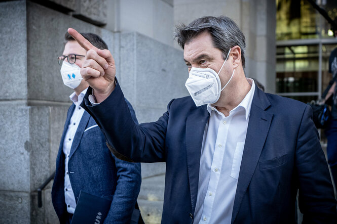 Söder mit Maske zeigt mit dem Zeigefinger auf etwas außerhalb des Bildes