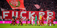 Team von RB Leipzig läuft auf den Rasen, Hintergrund Transparent mit Aufschrift "Fuck RB"