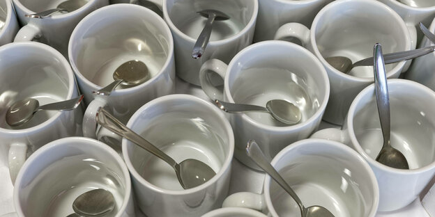 Zahlreiche Tassen eng nebeneinander, in denen ein Teelöffel liegt.