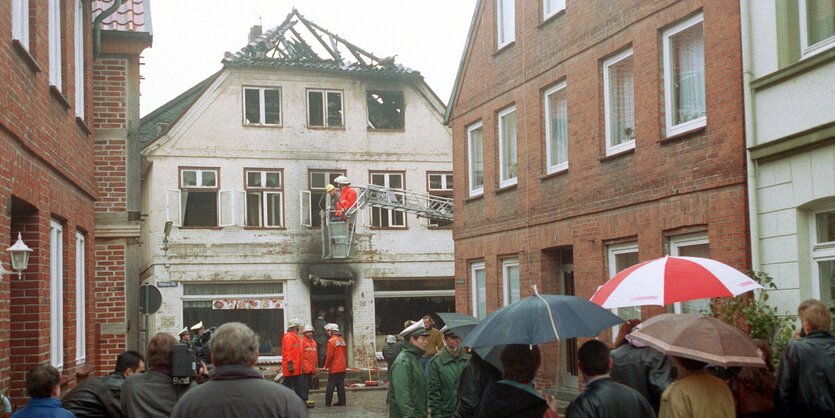 Menschen stehen vor einem Haus, an dem Brandspuren zu sehen sind