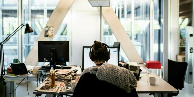 Eine Journalistin sitzt mit Kopfhörern an ihrem Arbeitsplatz in einer Redaktion