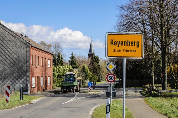 Ortsschild Keyenberg, Dorfstraße mit Kirche , ein Traktor fährt