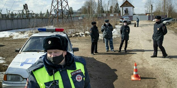 Russische Polizisten mit Auto vor einer Mauer.