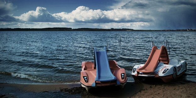 Zwei Tretboote, von der Sonne ausgebleicht, mit Rutsch an einem See