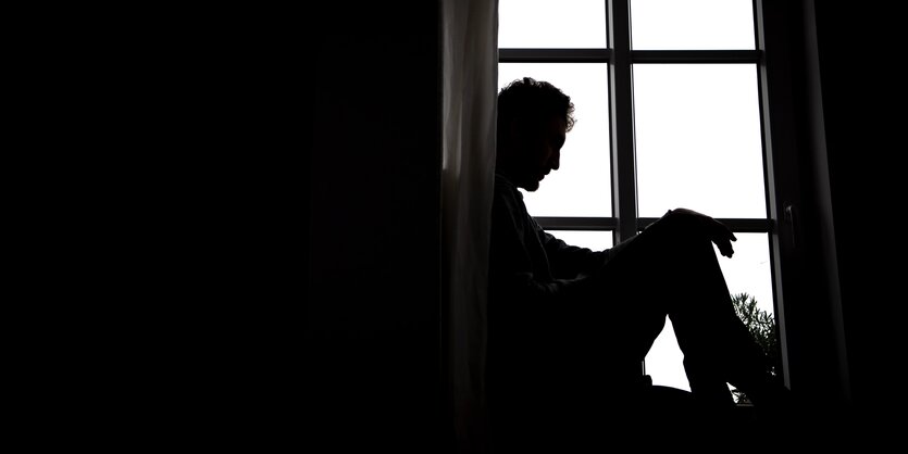 Trauernder Mann sizt im Schatten am Fenster