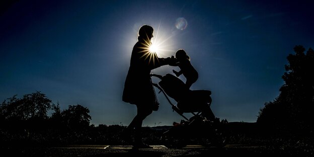Silhouette einer Mutter im Sinnen-Gegenlicht, die ihr Kind aus dem Kinderwagen hebt
