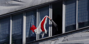 Eine Person winkt mit einer rot-weißem Flagge aus einem Fenster in Minsk