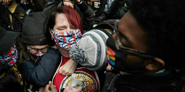 Eine Frau mit Mundschutz steht weinend in einer Menschenmenge und wird von anderen Demonstranten gehalten und umarmt