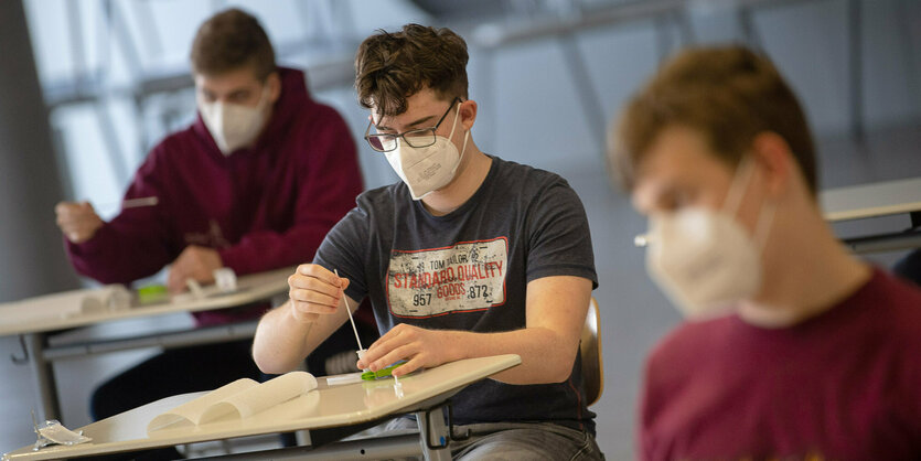 Jugendliche sitzen an Tischen. Sie tragen Masken