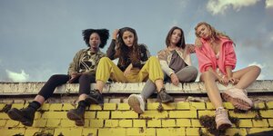 Die vier Protagonistinnen der TNT Serie Para - Wir sind King sitzen auf einer gelben Backsteinmauer