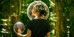 Mädchen steht in eiem Wald umgeben von einer Blase, sie hält einen Vogel in einer Blase