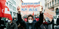 Ein Mann mit Maske hält auf einer Demonstration in Berlin ein Schild hoch. Darauf steht: Kostenloser Wohnraum für alle