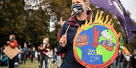 Eine Demonstration hält ein Schild, das eine brennende Erde zeigt, während einer Klima-Demo in Bonn
