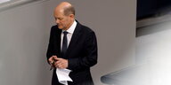 Olaf Scholz ist im Bundestag im Anzug und hält ein Blatt Papier