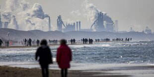 Menschen an einem Strand vor einer Fabrik