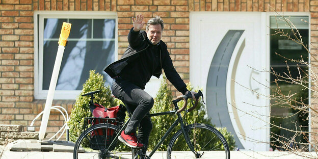 Robert Habeck sitzt auf einem Fahrrad in Flensburg und winkt