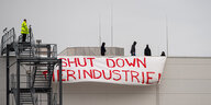 Menschen auf einem Hallendach, vor ihnen hängt ein Transparent mit der Aufschrift "Shut down Tierindustrie"